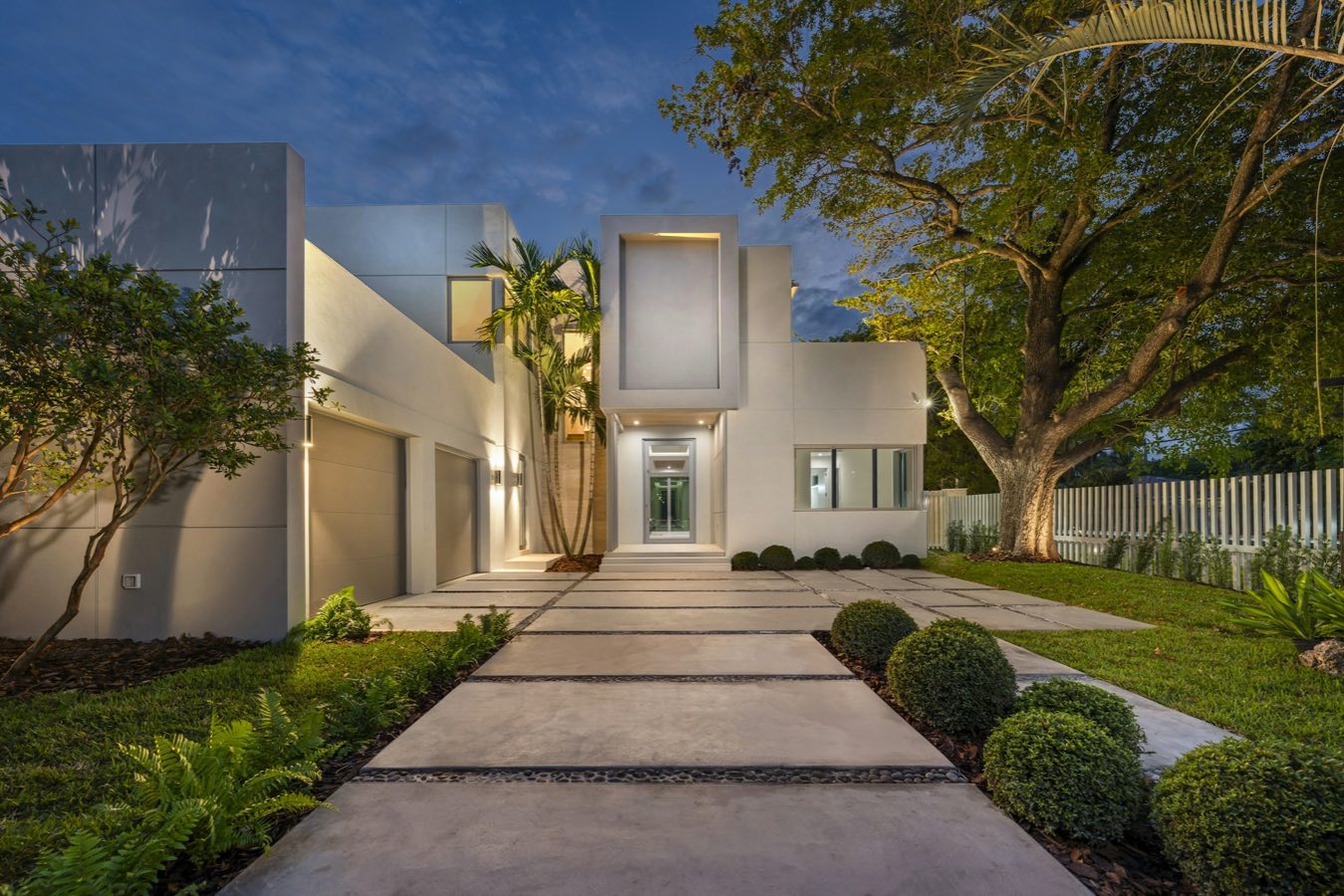 White modern house with a lit path at dusk